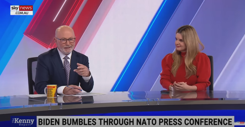 a man and a woman talking on the news with the headline "Biden Bumbles Through NATO Press Conference"