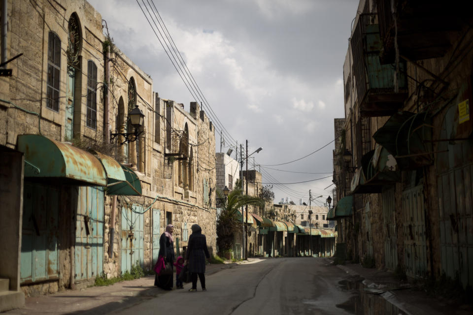 In this Wednesday, March 6, 2019 photo, Palestinian women walk in a street where shops have been closed for a few years in the Israeli controlled part in the West Bank city of Hebron. The Falic family, owners of the ubiquitous chain of Duty Free America shops, fund a generous, and sometimes controversial, philanthropic empire in Israel that stretches deep into the West Bank.The family supports many mainstream causes as well as far right causes considered extreme even in Israel. (AP Photo/Ariel Schalit)