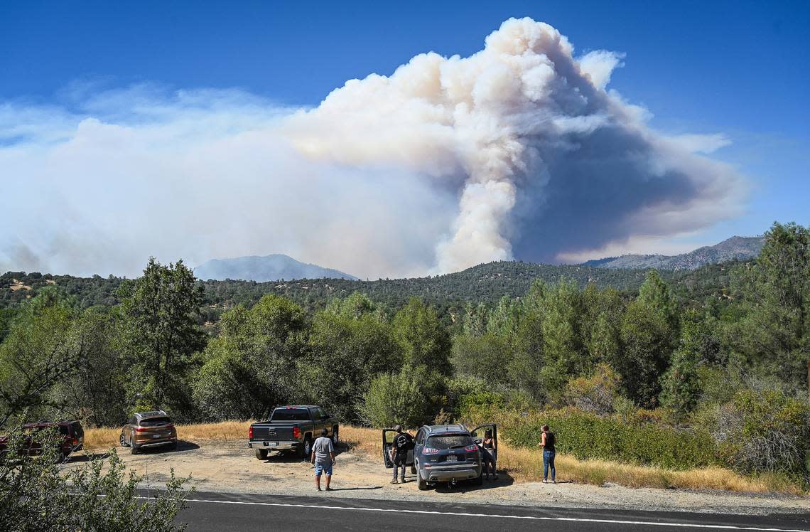 Local residents watch from the Highway 49 roadside as plumes of smoke from the Oak Fire erupt from a mountainside east of Mariposa on Saturday, July 23, 2022.