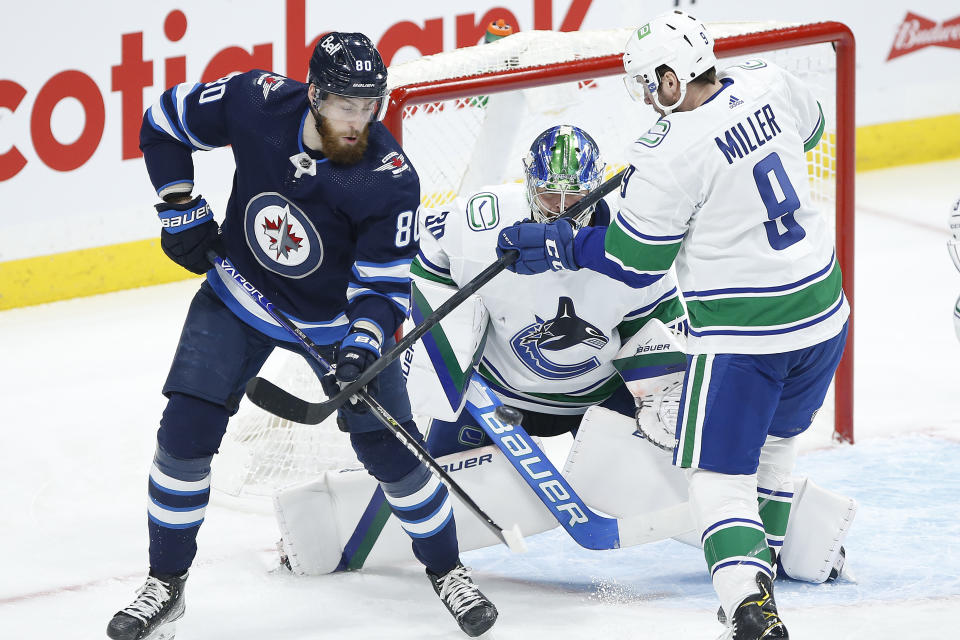 Winnipeg Jets' Pierre-Luc Dubois (80) looks to tip the puck past Vancouver Canucks goaltender Spencer Martin (30) as JCanucks' .T. Miller (9) defends during first-period NHL hockey game action in Winnipeg, Manitoba, Thursday, Jan. 27, 2022. (John Woods/The Canadian Press via AP)