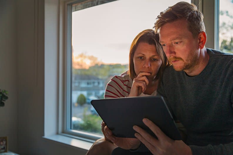 Worried-looking couple looking at a tablet together.