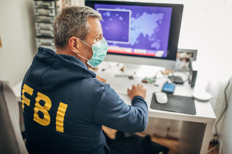 One senior FBI agent with protective mask working on the computer in the office. Fight against coronavrus.