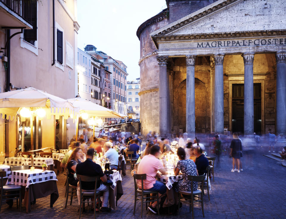 Outdoor cafe scene with patrons dining near a historical building at dusk