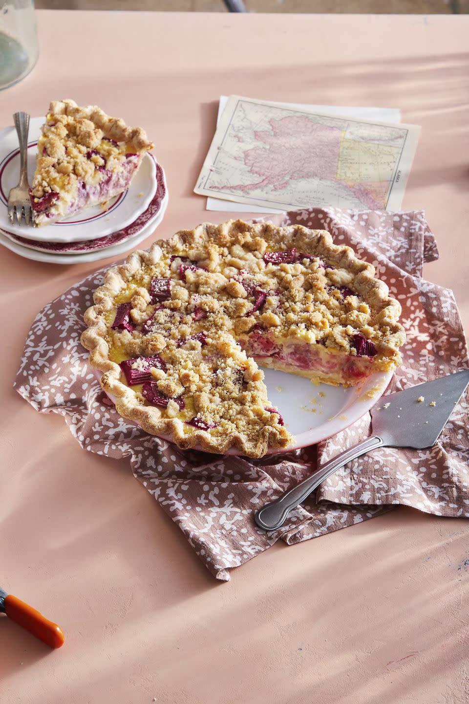 rhubarb custard pie with crumble topping in a white pie plate and a slice removed on a small plate to the side