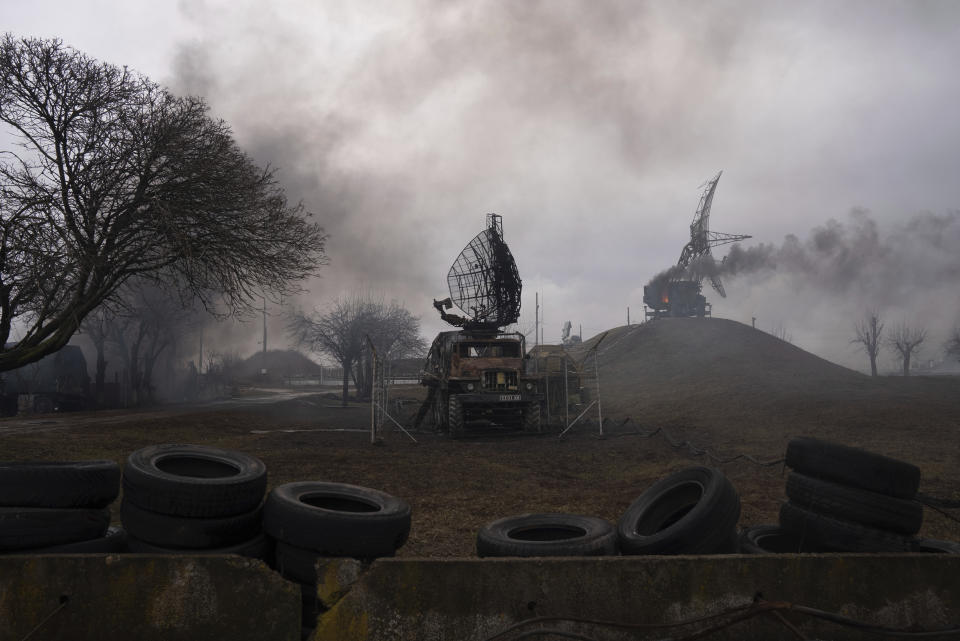 Smoke surrounds two radar structures, with a row of truck tires laid out in the foreground.