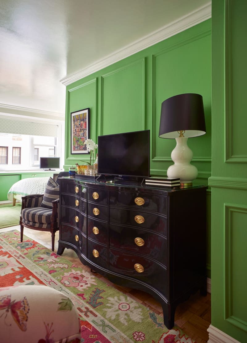 Television and lamp on top of dark dresser in green living room area.