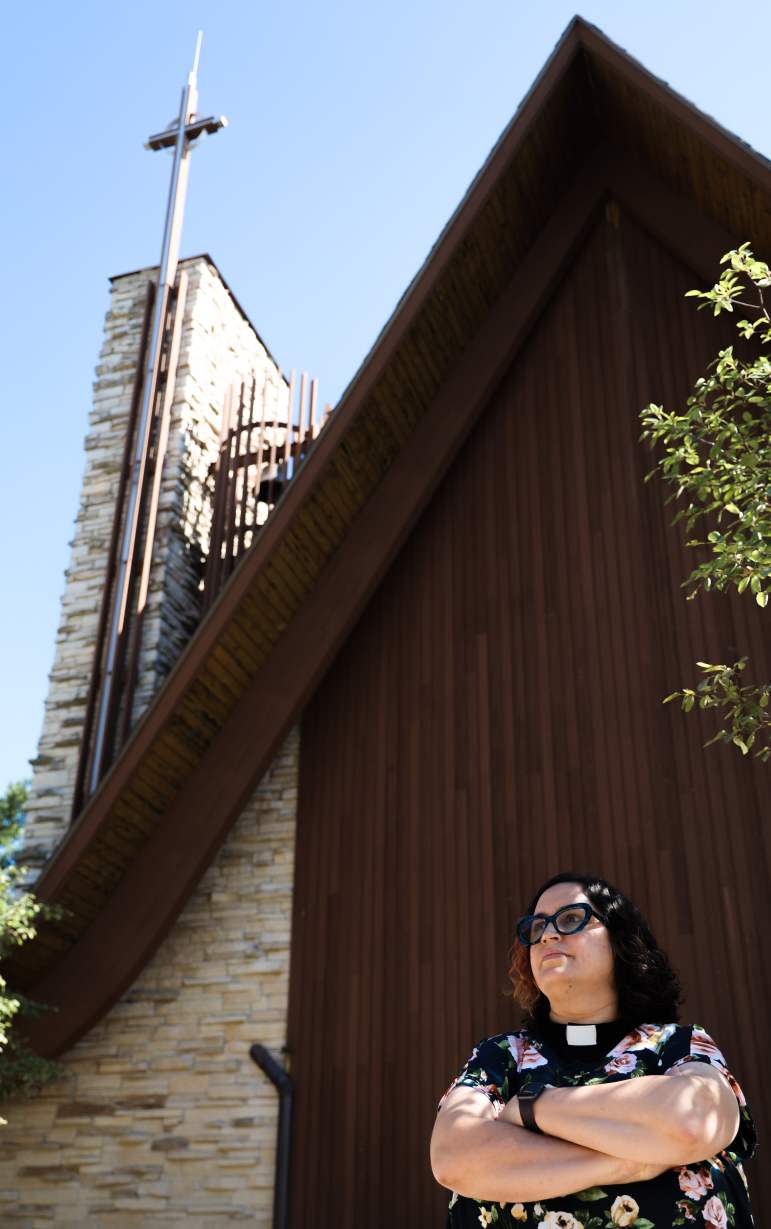 The Rev. Miranda Hasset stands outside St. Dunstan’s Episcopal Church in Madison, Wis., where she has been rector for 11 years. The church has worked to acknowledge and compensate Native people for the land under the church that was taken from them in the treaty of 1832. Taken Aug. 26, 2022. (Amena Saleh / Wisconsin Watch)