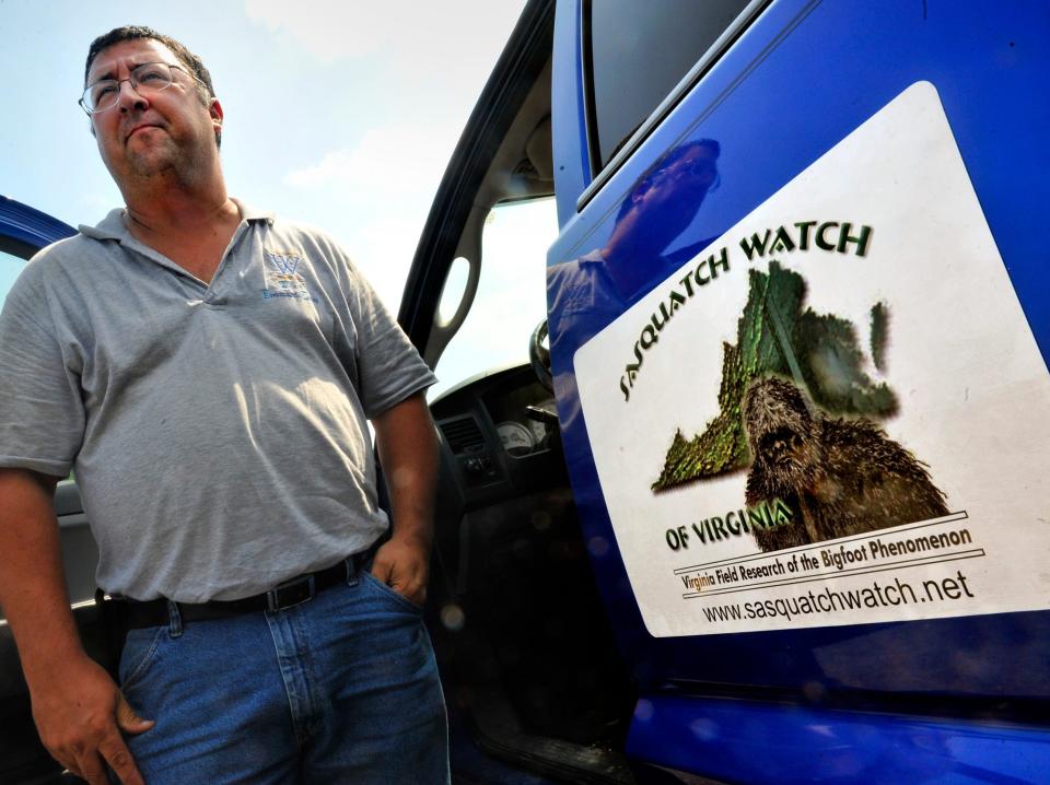 A man stands next to a truck with a decal that says Sasquatch Watch