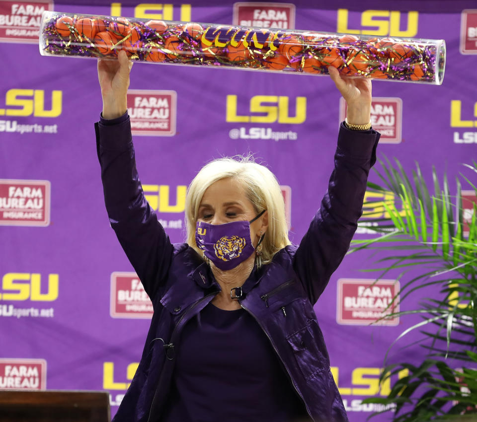 Kim Mulkey raises a cylinder filled with LSU colored confetti and mini basketballs above her head.