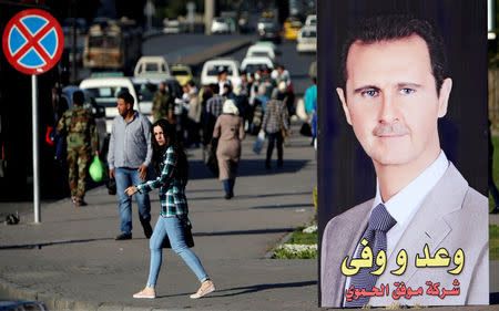 FILE PHOTO:A woman walks near a picture of Syrian President Bashar al Assad in Damascus, Syria April 15, 2018. REUTERS/Ali Hashisho/File Photo