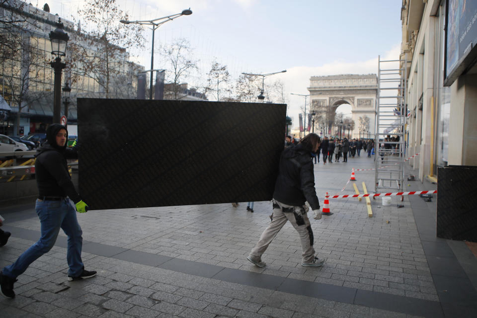 Workers carry a large plank to protect shop a window on the Champs-Elysees avenue in Paris, Friday, Dec.14, 2018. Anticipating a fifth straight weekend of violent protests, Paris' police chief said Friday that armored vehicles and thousands of officers will be deployed again in the French capital this weekend. (AP Photo/Francois Mori)