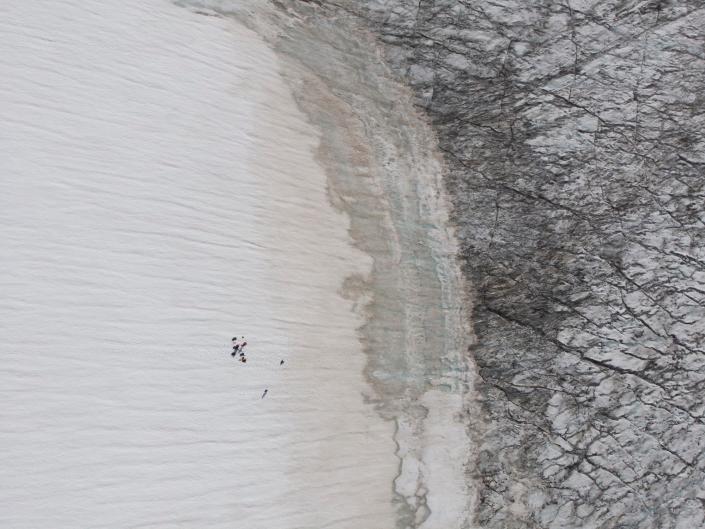 drone image shows people walking across white snow toward black cracked snow