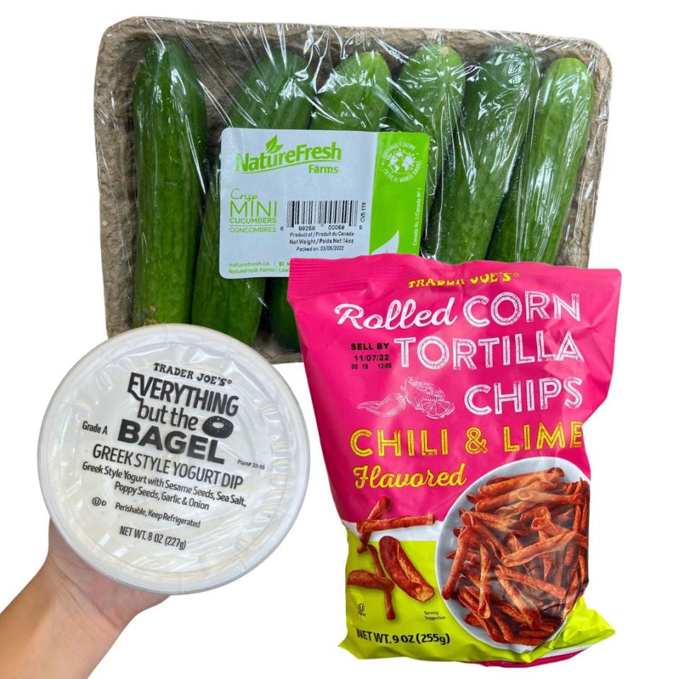 A shrink-wrapped package of cucumbers, a bag of rolled corn tortilla chips, and a container of Everything But the Bagel dip