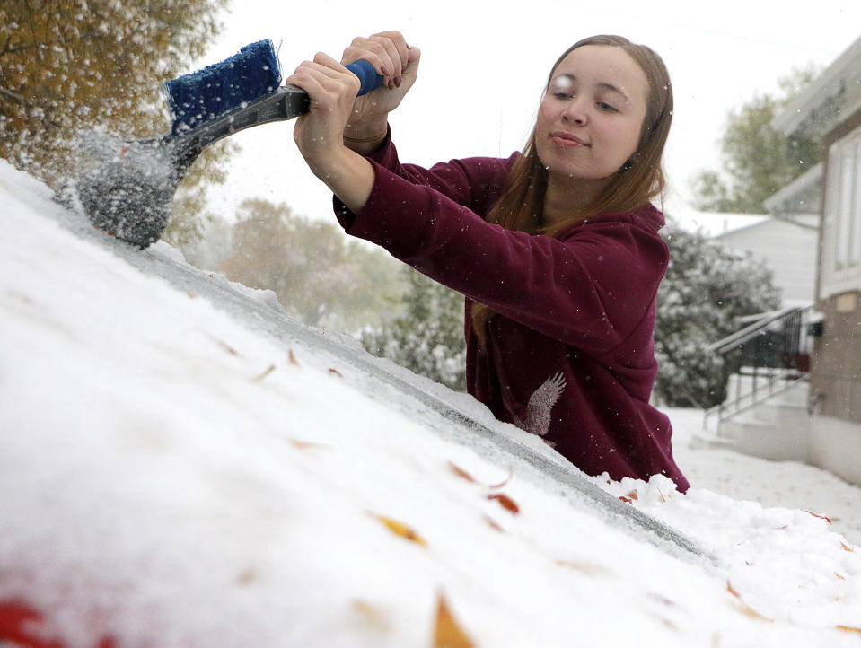 MaKenzie Gregory scrapes ice off her vehicle's front windshield as snow continues to fall in Scottsbluff, Neb., Thursday, Oct. 10, 2019. Gregory said she didn't know it was going to snow that much. (Lauren Brant/The Star-Herald via AP)