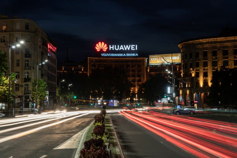 Cars drive past a Huawei logo on a building in central Belgrade