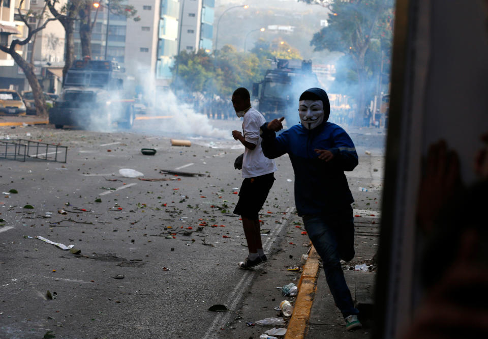 Opposition demonstrators who were throwing stones at the Bolivarian National Police run from tear gas fired by police during clashes in Caracas, Venezuela, Saturday, Feb. 15, 2014. Venezuelan security forces backed by water tanks and tear gas are dispersing groups of anti-government demonstrators who blocked Caracas' main highway Saturday evening. (AP Photo/Fernando Llano)