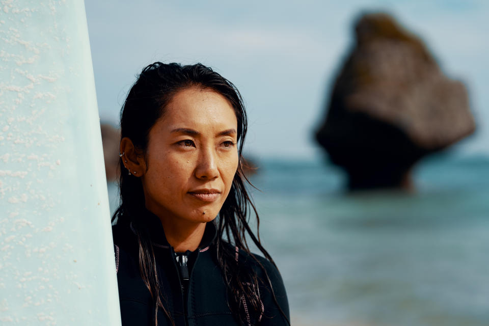 Portrait of a mature female athlete with her surfboard standing on a beach in Japan