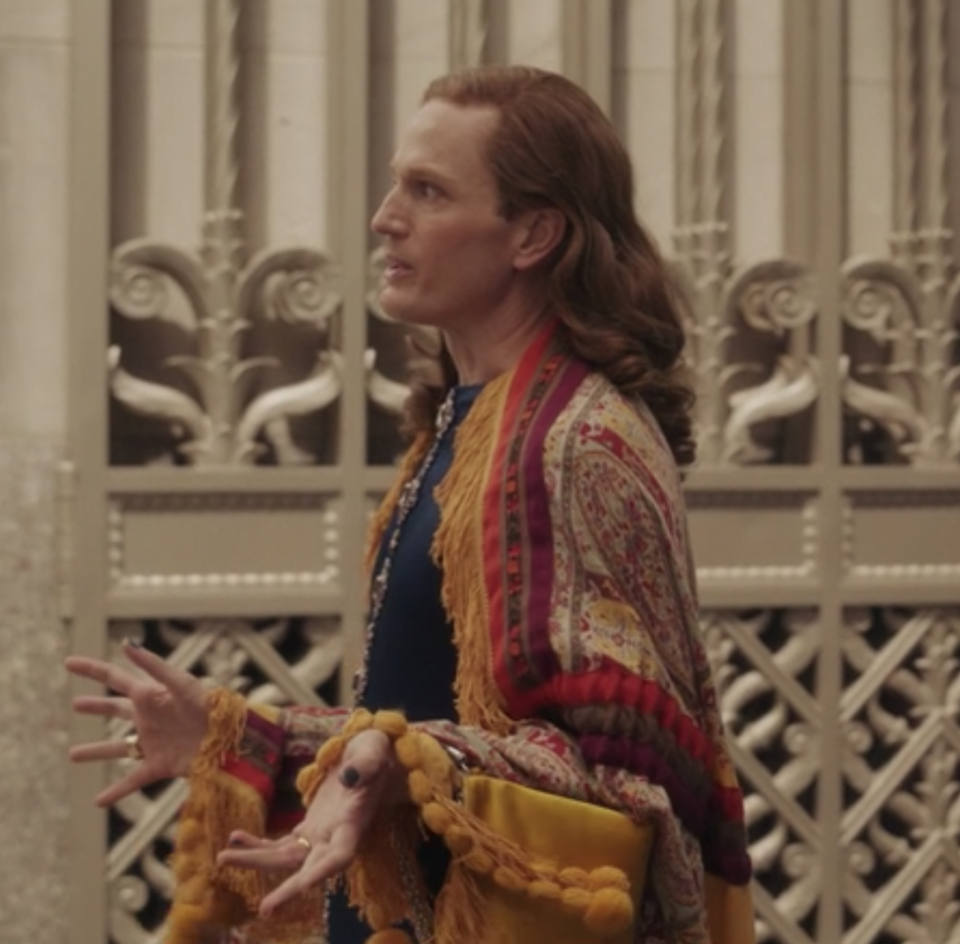 Gideon Wolfe wears a brightly colored patterned long cape over a dark shirt
