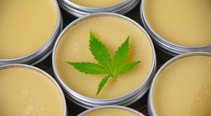 A marijuana leaf rests on top of little tins filled with a balm.