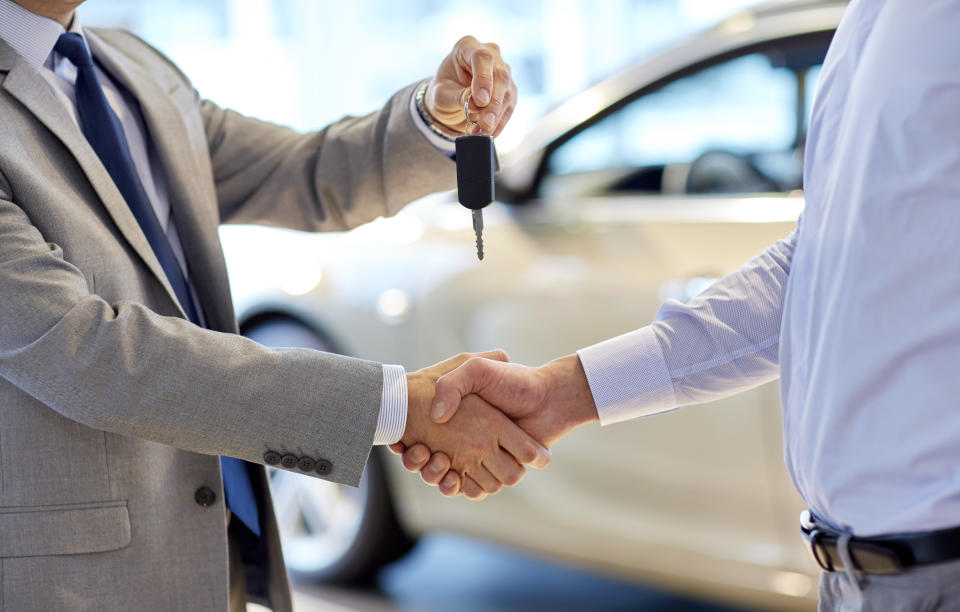 A customer receiving the keys to his new car from a salesman.