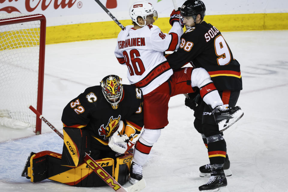 Carolina Hurricanes forward Teuvo Teravainen, center, is checked by Calgary Flames defenseman Ilya Solovyov, right, into Flames goalie Dustin Wolf, left, during second-period NHL hockey game action in Calgary, Alberta, Thursday, Dec. 7, 2023. (Jeff McIntosh/The Canadian Press via AP)