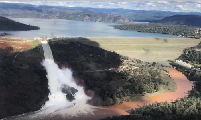 Water pours from an open spillway coming from a full lake with a dam.