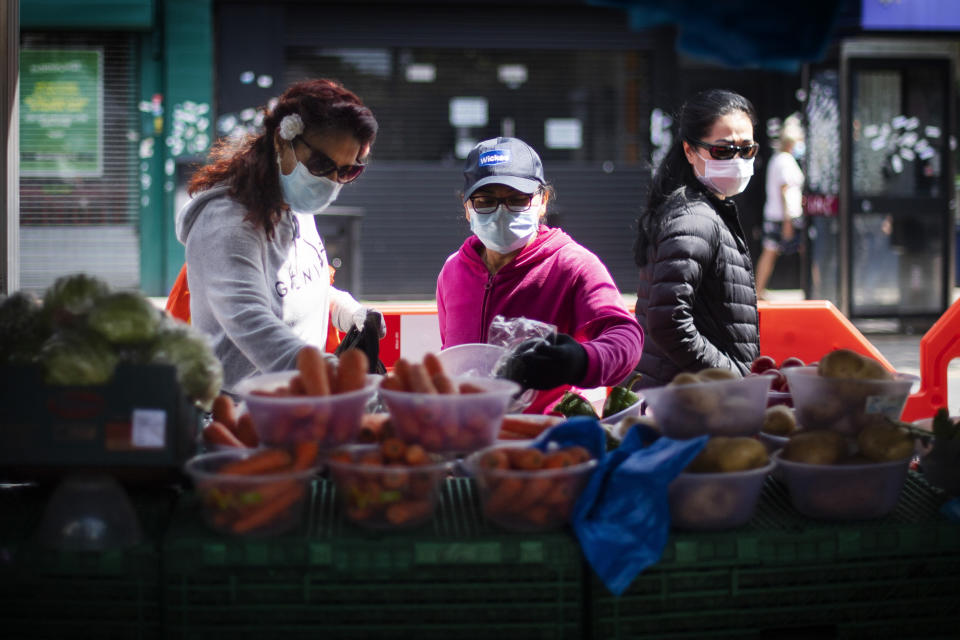 Three women wearing protective face masks buy fruit and vegetables at a high street market stall in East Ham, east London, as the UK continues in lockdown to help curb the spread of the coronavirus.