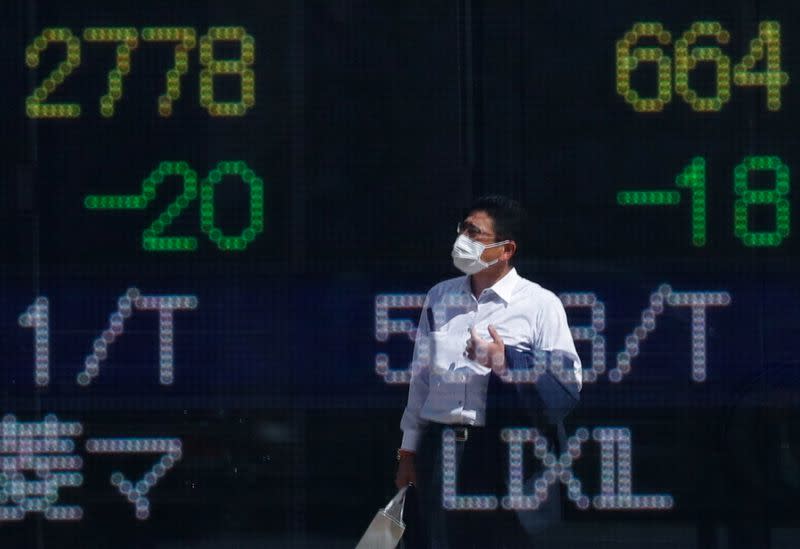 FILE PHOTO: A man wearing a protective mask is reflected on an electronic board displaying stock prices outside a brokerage in Tokyo