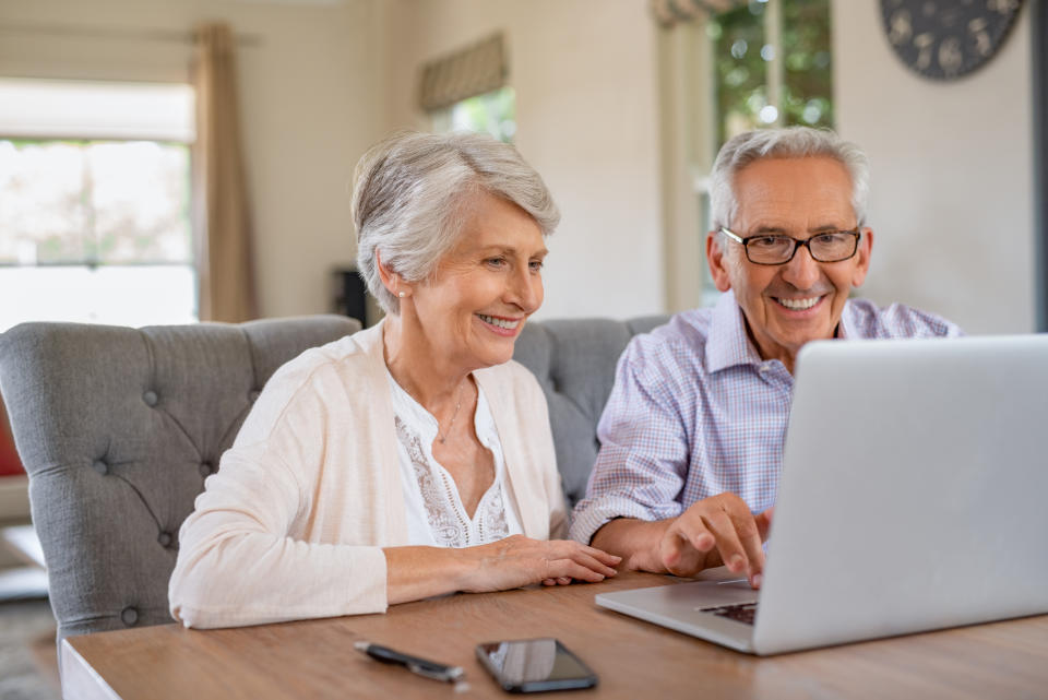 Ein Seniorenpaar sitzt gemeinsam vor einem aufgeklappten Laptop.
