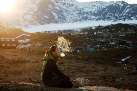 A young girl sits on a stone and smokes in the late evening sunshine above the town of Tasiilaq, Greenland, June 18, 2018. REUTERS/Lucas Jackson