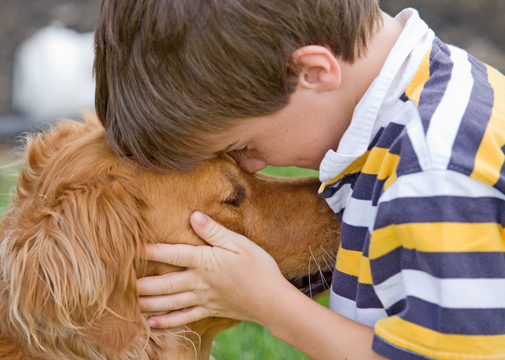 Five-year-old boy puts his forehead on a dog's head, holding the dog's face in his hands. 