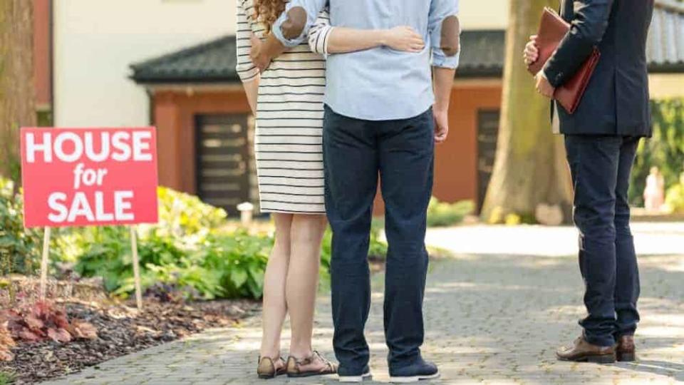 edit Back view of hugging couple standing with real estate agent in front of house for sale