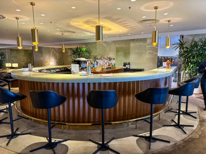 A round bar with black high-top stools is positioned in the center of the lounge at Cathay Pacific's The Pier, a first-class lounge at Hong Kong International Airport