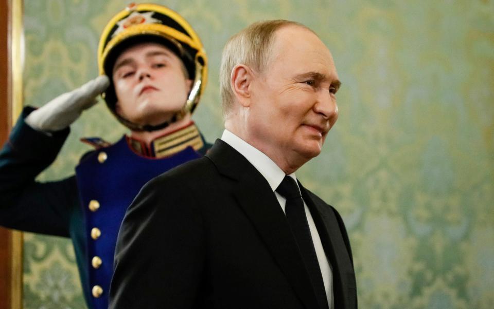 Vladimir Putin,in a black suit and tie, with a guard soldier behind him in dress uniform, saluting