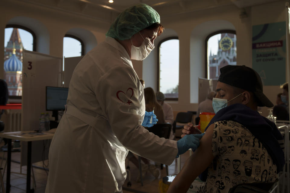 A medical worker administers a shot of Russia's Sputnik Lite coronavirus vaccine at a vaccination center in the GUM, State Department store, in Red Square with the Spasskaya Tower, right, and the St. Basil Cathedral in the background, in Moscow, Russia, Tuesday, Oct. 26, 2021. The daily number of COVID-19 deaths in Russia hit another high Tuesday amid a surge in infections that forced the Kremlin to order most Russians to stay off work starting this week. (AP Photo/Pavel Golovkin)