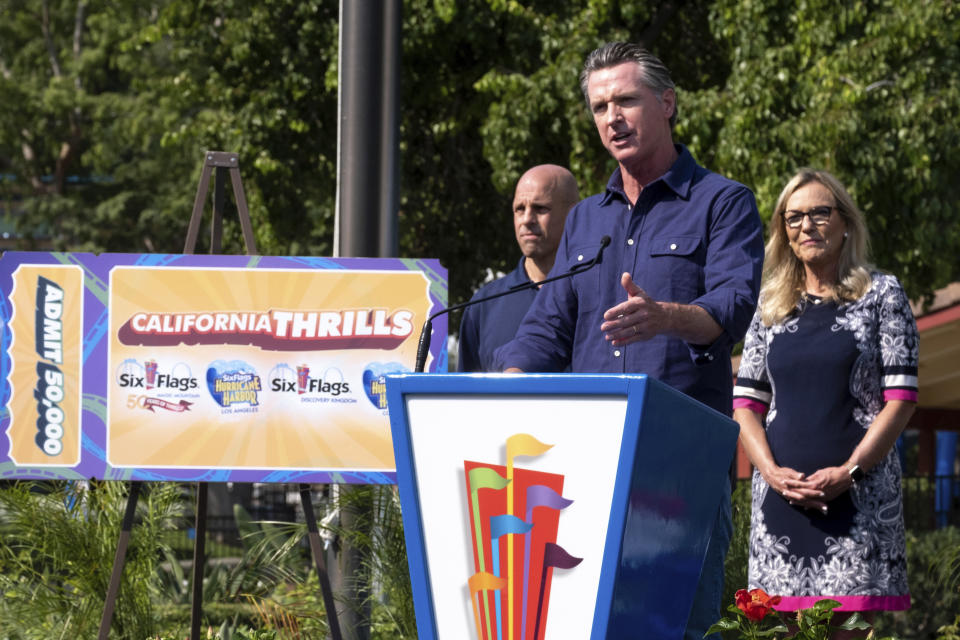 California Gov. Gavin Newsom welcomes the public to Six Flags Magic Mountain in Santa Clarita, Calif. Wednesday, June 16, 2021. At left, is Michael Spanos, President of Six Flags, at right is LA county supervisor Kathryn Barger. Newsom continued his tour of the state after lifting most COVID-19 restrictions Tuesday. (David Crane/The Orange County Register via AP)