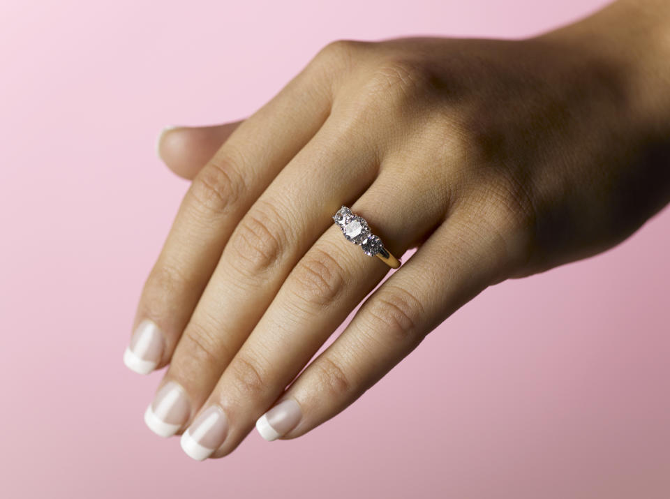 A person's hand displaying an engagement ring with a prominent gemstone