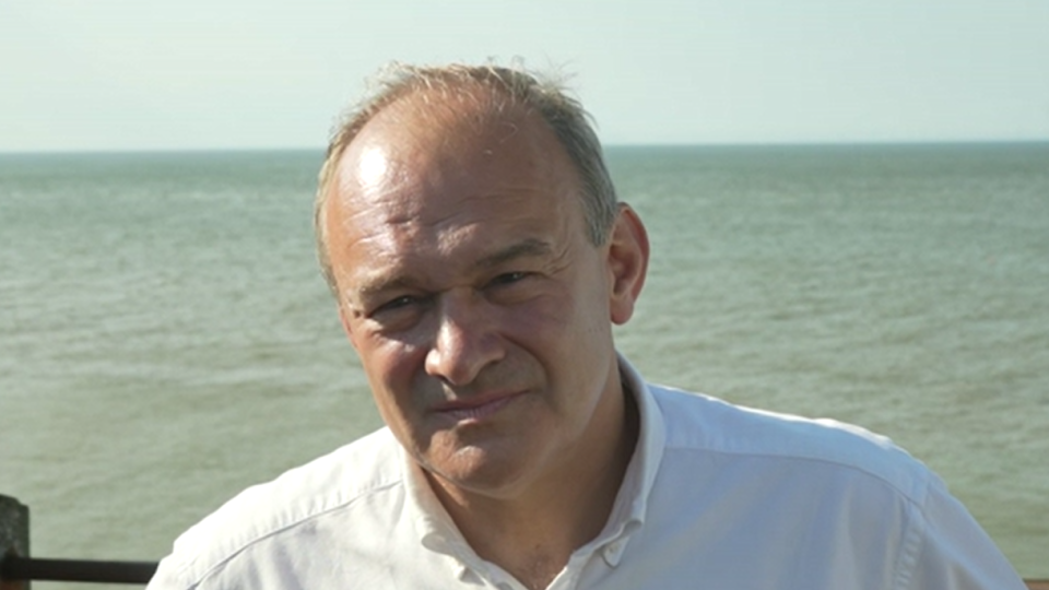 Sir Ed Davey in a white shirt, with the sea behind him
