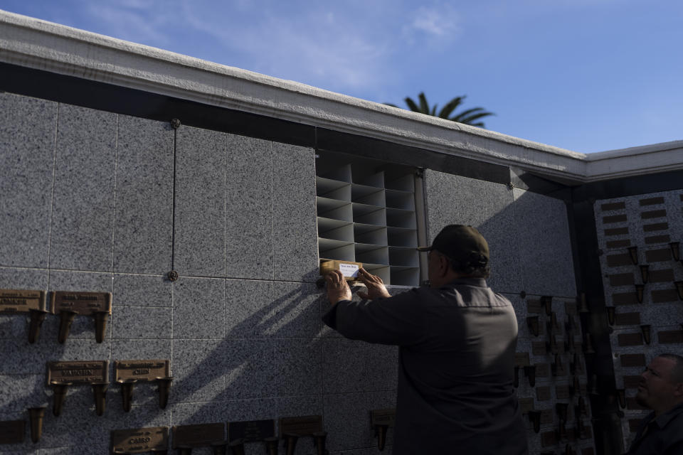 Cemetery worker Jorge Alberto Cortez places an urn holding the ashes of an unclaimed Los Angeles County resident into a columbarium at Odd Fellows Cemetery in Los Angeles on Thursday, Dec. 14, 2023. (AP Photo/Jae C. Hong)