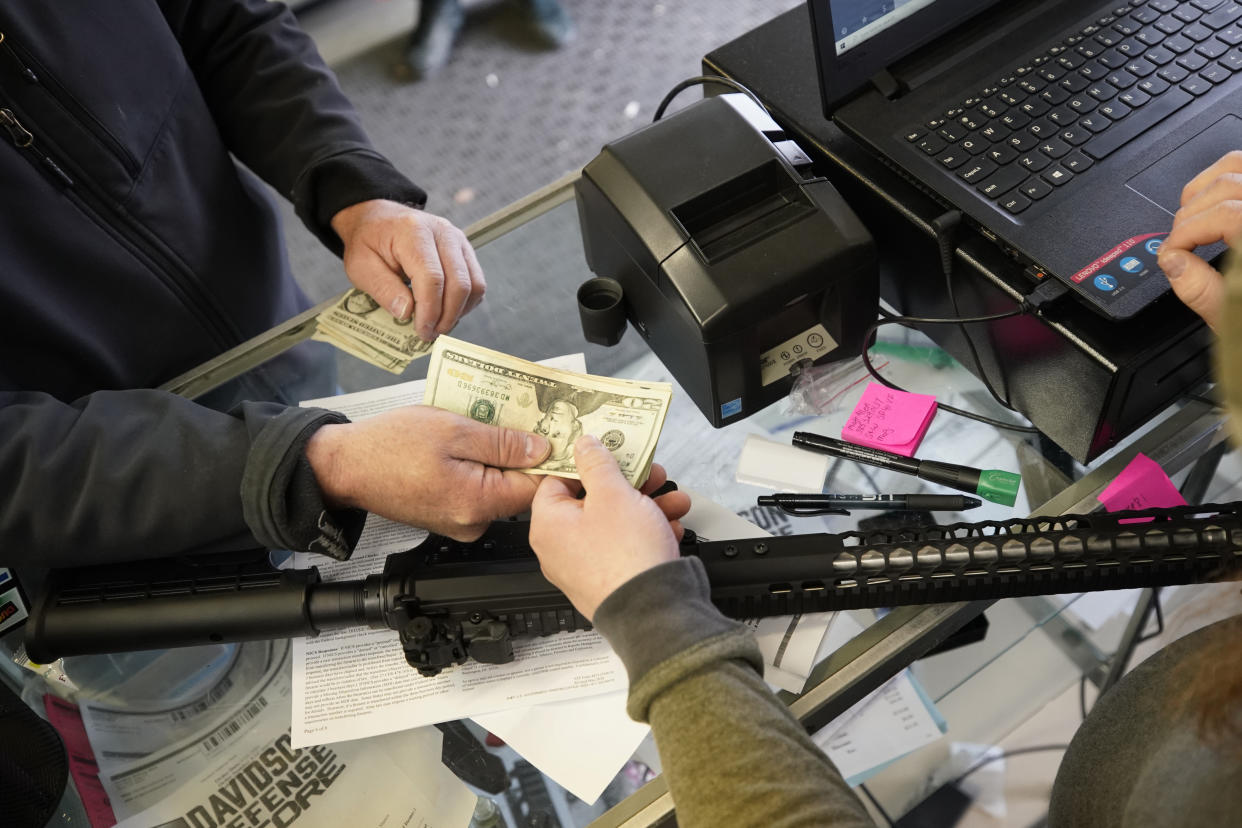 At a gun store counter, a customer hands over cash for an AR-15 rifle.