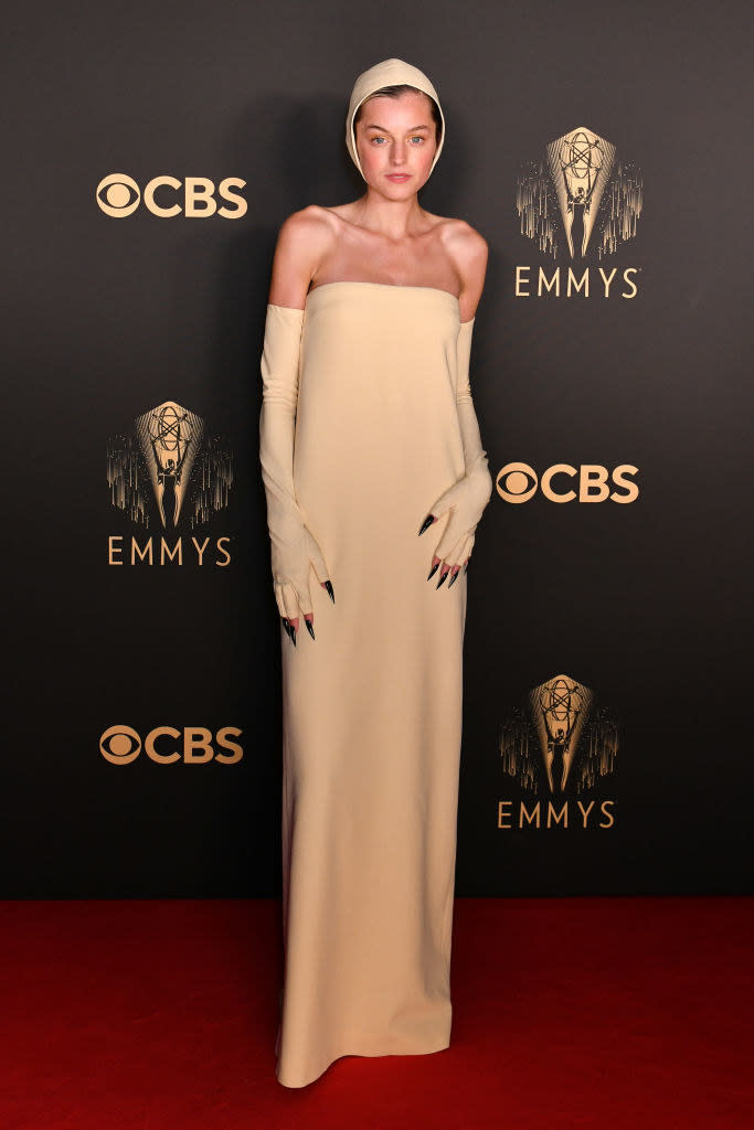Emma Corrin on the red carpet in an all beige gown and matching bonnet