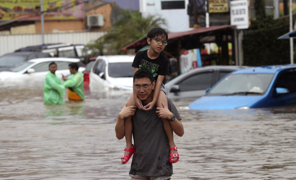 A man carrying a boy wades through floodwaters at Jatibening on the outskirt of Jakarta, Indonesia, Wednesday, Jan. 1, 2020. Severe flooding hit Indonesia's capital just after residents celebrating New Year's Eve, forcing a closure of an airport and thousands of inhabitants to flee their flooded homes. (AP Photo/Achmad Ibrahim)