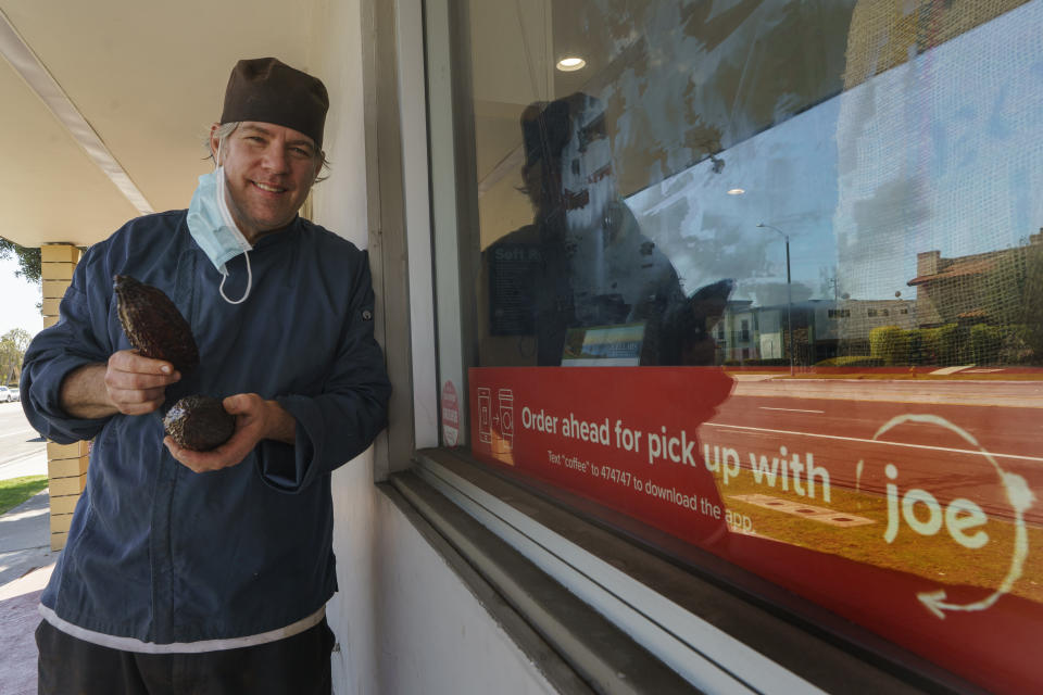 Jeffray Gardner, the owner of Marsatta Chocolate holds cacao fruit pods outside his flagship store in Torrance, Calif., Sunday, March 28, 2021. Restaurants and delivery companies remain uneasy partners, haggling over fees and struggling to make the service profitable for themselves and each other. Gardner says he probably loses money on the one or two delivery orders he gets each day. But he’s still happy to work with delivery companies because they help him reach a wider audience. (AP Photo/Damian Dovarganes)