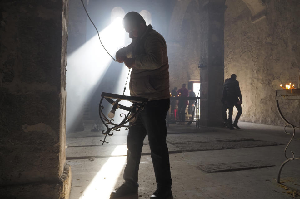 A man removes lamps inside a church of the Dadivank, an Armenian Apostolic Church monastery dating to the 9th century, as ethnic Armenians leave the separatist region of Nagorno-Karabakh to Armenia, Saturday, Nov. 14, 2020. The territory is to be turned over to Azerbaijan on Sunday as part of territorial concessions in an agreement to end six weeks of intense fighting with Armenian forces. Hundreds of thousands of Azeris were displaced by the war that ended in 1994. It is unclear when any civilians might try to settle in Karvachar — which will now be known by its Azeri name Kalbajar — or elsewhere. (AP Photo/Dmitry Lovetsky)