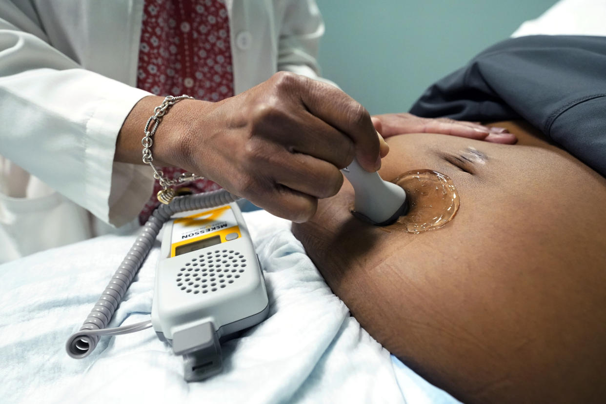 A doctor uses a handheld Doppler probe on the belly of a pregnant woman lying back to measure the heartbeat of the fetus.