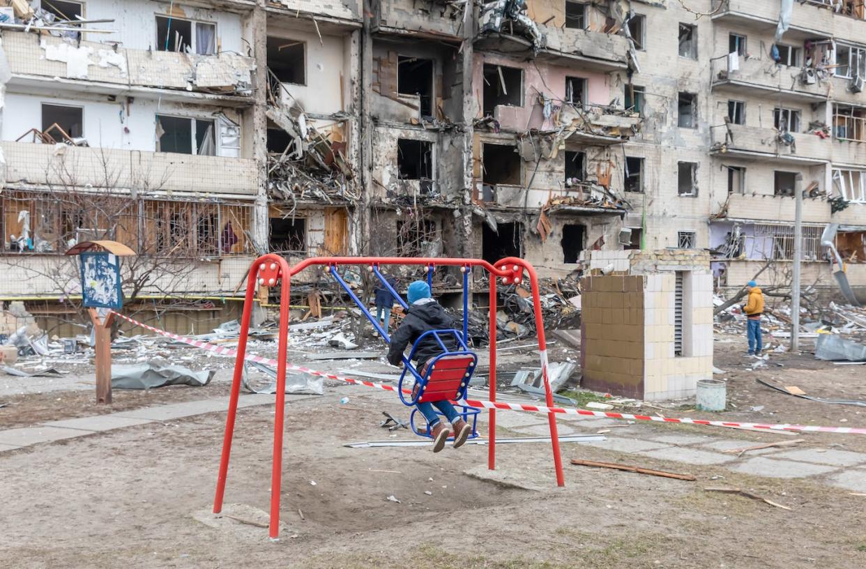 Niño en un columpio contra un edificio residencial dañado por un cohete ruso en una zona residencial de Kiev. <a href="https://www.shutterstock.com/es/image-photo/kyiv-ukraine-feb-25-2022-war-2130296600" rel="nofollow noopener" target="_blank" data-ylk="slk:Drop of Light / Shutterstock;elm:context_link;itc:0;sec:content-canvas" class="link ">Drop of Light / Shutterstock</a>