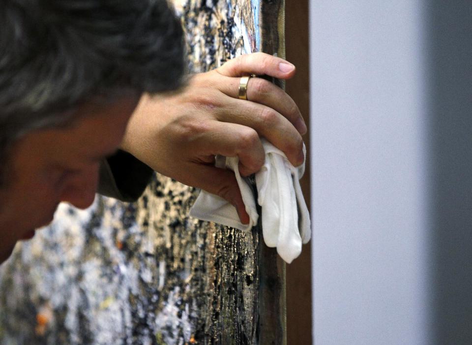 Nicholas Dorman, chief conservator for the Seattle Art Museum, holds gloves against the canvas as he turns Jackson Pollock's painting Sea Change around during a news conference about his on-going restoration work of the art Tuesday, Nov. 27, 2012, at the museum in Seattle. The celebrated piece, part of SAM's permanent collection, was painted in 1947 and altered in 1970 with a coat of varnish. Dorman is several months into the restoration work, which is complicated by the uneven surface and multiple layers of media, including several types of paint and imbedded gravel. The restoration is sponsored by Bank of America's Art Conservation Project, which enabled SAM staff and consulting experts to undertake a study of the original materials and evaluate the impact of materials used in conservation treatments. (AP Photo/Elaine Thompson)