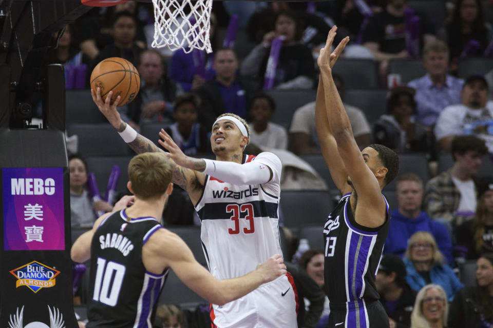 Washington Wizards forward Kyle Kuzma (33) lays the ball up between Sacramento Kings forward Domantas Sabonis (10) and forward Keegan Murray during the second half of an NBA basketball game in Sacramento, Calif., Monday, Dec. 18, 2023. The Kings won 143-131. (AP Photo/Randall Benton)