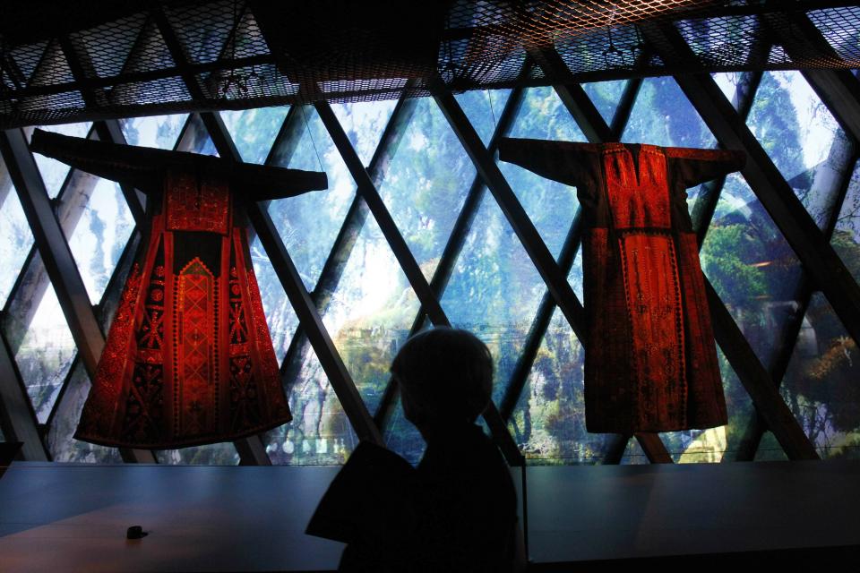 FILE - In this Feb. 7, 2011 file photo, a woman views traditional Palestinian thobes during the exhibition "Women in Orient" at the Quai Branly Museum in Paris, France. The thobe, a brightly embroidered robe for women, has long been a staple of Palestinian life, sewn by village women and worn at weddings and parties. Now it’s gaining prominence as a softer symbol of Palestinian nationalism, competing with the classic keffiyeh. (AP Photo/Christophe Ena, File)