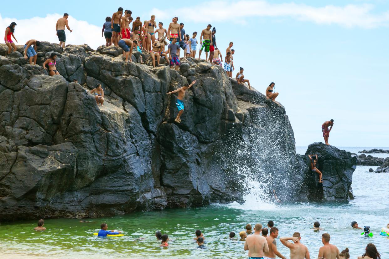 Crowd of people enjoys Jump Rock, Waimea Bay, Oahu Hawaii.